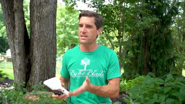 Still from a By The Blade video: the founder in a branded green tee explains a project from a client's garden.