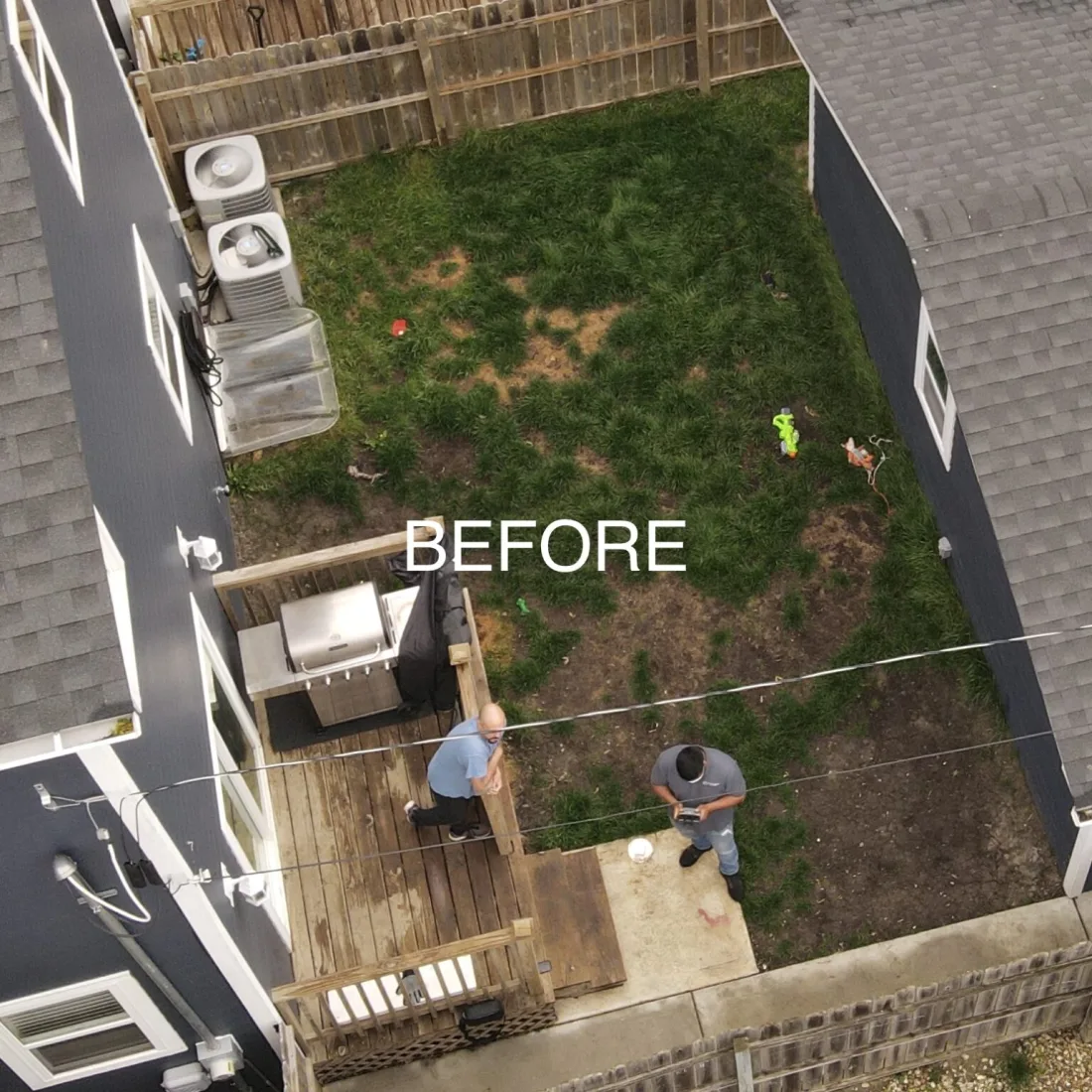 A backyard before the build: patchy grass, bare dirt and a weathered wooden deck.